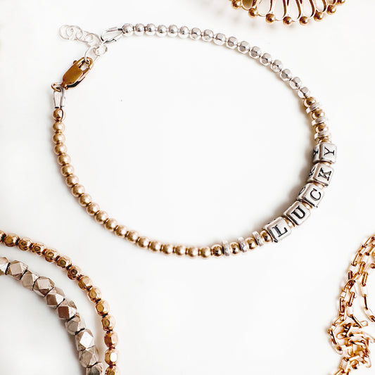 Beaded bracelet in sterling silver and 14k gold that says Lucky in sterling silver letters