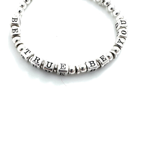 Silver beaded bracelet with 'BE TRUE' engraved on a white background