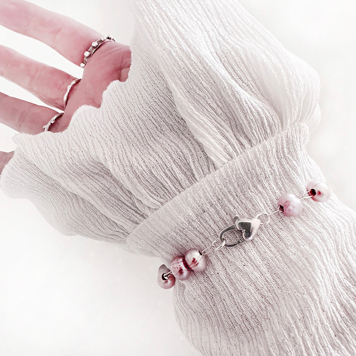 A Pink pearl bracelet with a sterling silver heart closure on a wrist