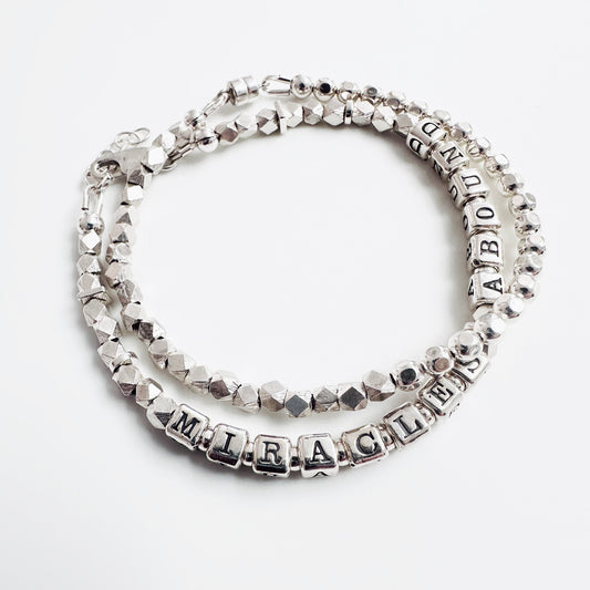 Sterling Silver bracelet spelling out the message "Miracles Abound" shown with sterling silver stacking bracelet