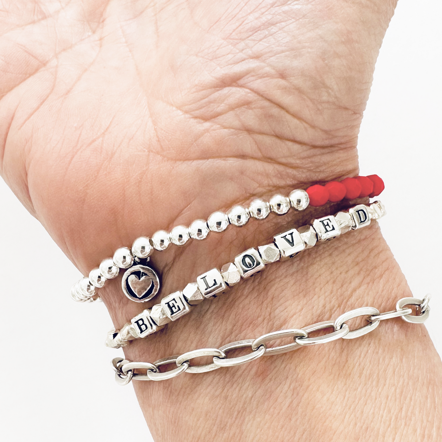 Beloved Love Bracelet in all sterling silver and a heart clasp, and a matching red and silver heart bracelet shown on woman's wrist